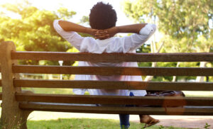Woman sits on a park bench looking at trees, birds, and nature