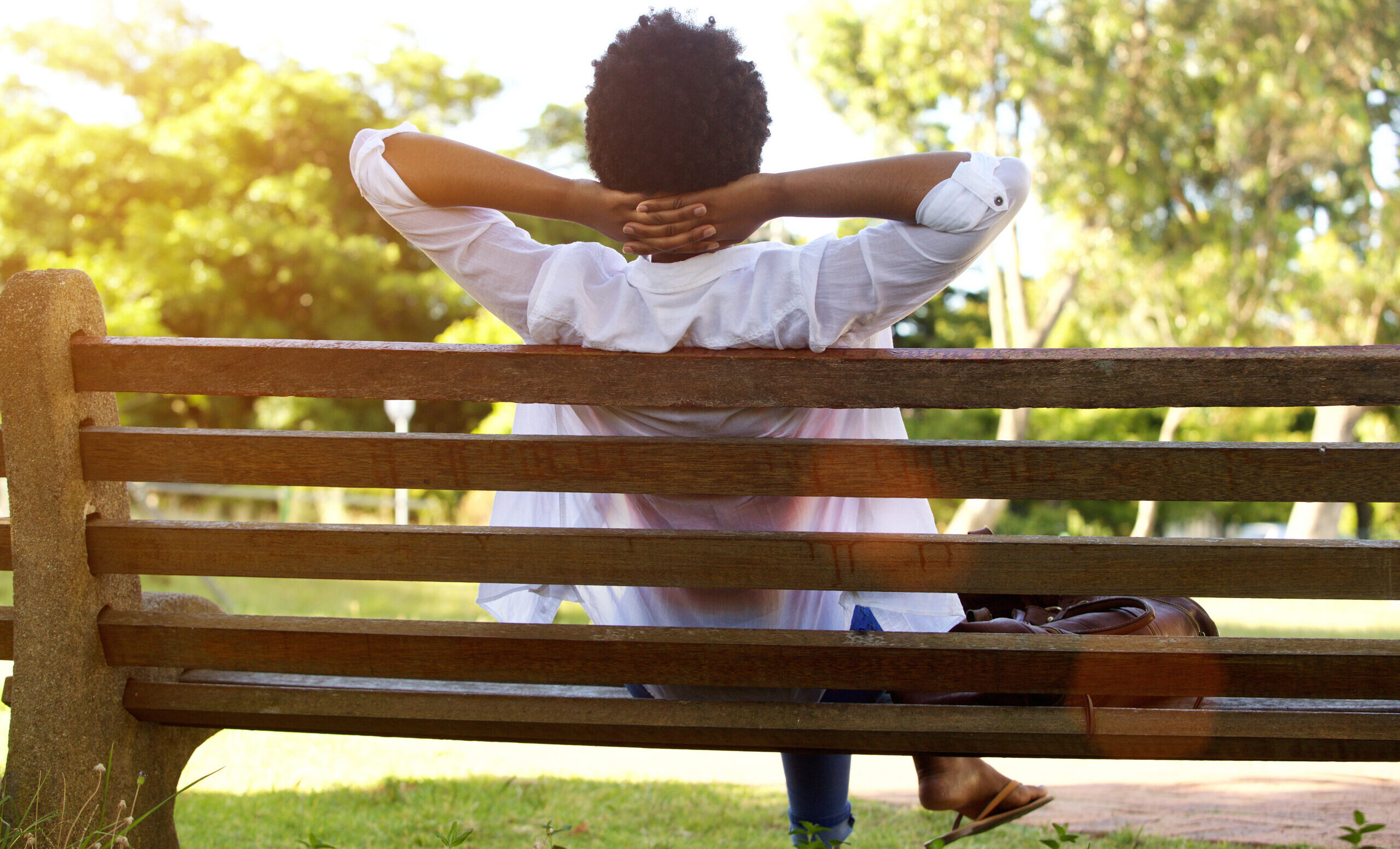 Woman sits on a park bench looking at trees, birds, and nature
